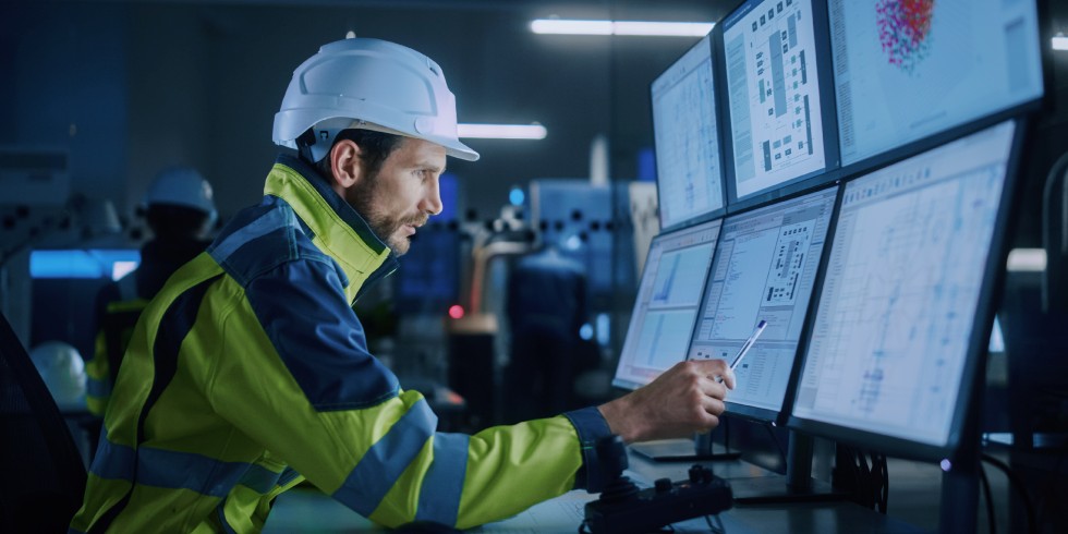 Industry 4.0 Modern Factory: Facility Operator Controls Workshop Production Line, Uses Computer with Screens Showing Complex UI of Machine Operation Processes, Controllers, Machinery Blueprints