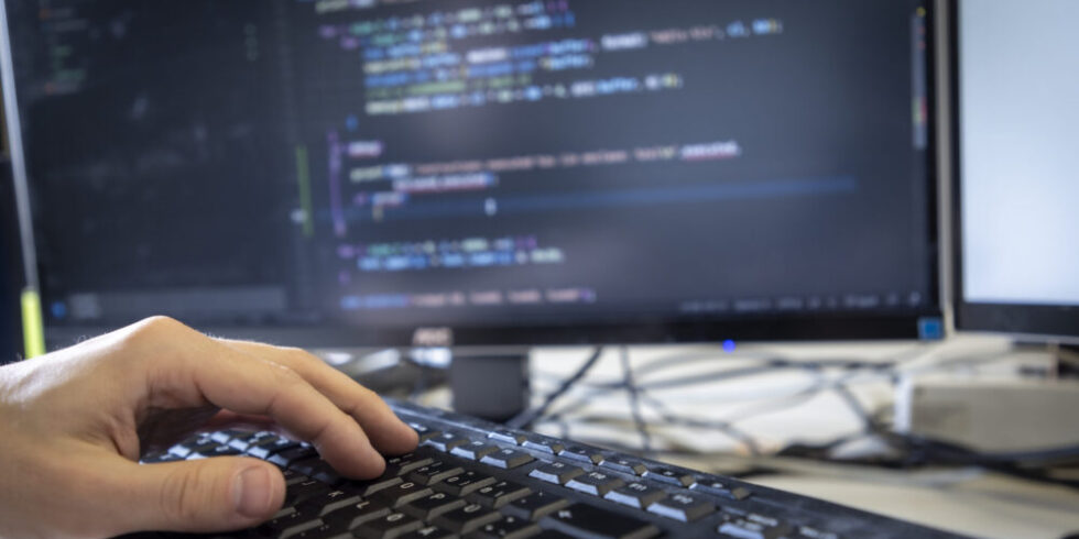 Hand auf Tastatur mit Computer-Monitor im Hintergrund