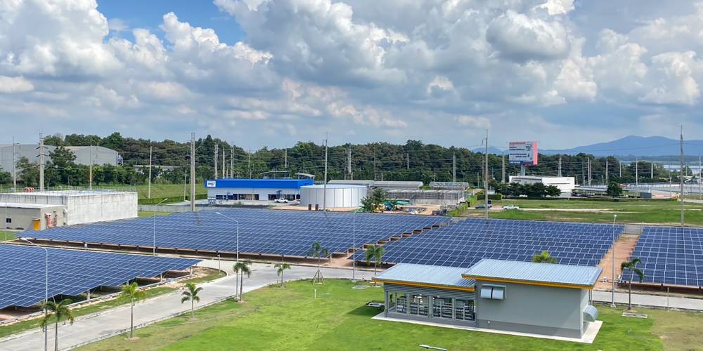 PV-Freiflächen-Anlagen mit Betriebsgebäuden, Bergketten und Wald, bewölkter Himmel