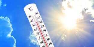 Thermometer zeigt heiße Temperaturen an vor blauem Himmel und strahlender Sonne