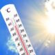 Thermometer zeigt heiße Temperaturen an vor blauem Himmel und strahlender Sonne