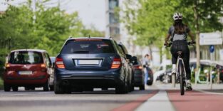 Mensch auf dem Fahrrad und auf dem Radweg fahrend während die Autos daneben unterwegs sind.