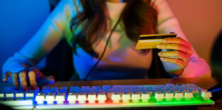 Eine Gamerin tippt aus einer Tastatur und hält eine Kreditkarte in der anderen Hand.