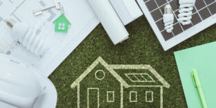 Eine Hauszeichnung auf Kunstrasen und drei Energiesparlampen.