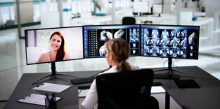Eine Ärztin sitzt an einem Tisch mit drei Monitoren.