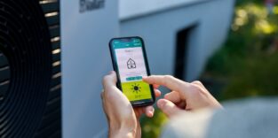 Frau hält ein Smartphone in den Händen, über das sie ihre Wärmepumpe und das Laden des Elektroautos steuern kann.