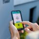 Frau hält ein Smartphone in den Händen, über das sie ihre Wärmepumpe und das Laden des Elektroautos steuern kann.