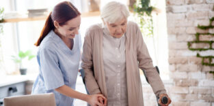 Eine Pflegerin hilft einer älteren Frau auf Krücken.