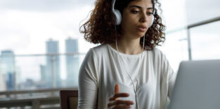 Junge Frau mit Kopfhörern arbeitet am Laptop in moderner Umgebung.