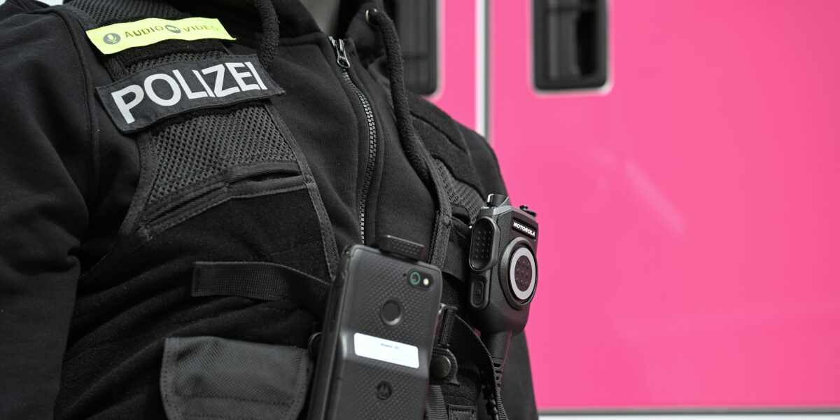 Eine Puppe mit Polizei-Unform steht auf der Digitalmesse Digital X vor einem Containerstand der Deutschen Telekom