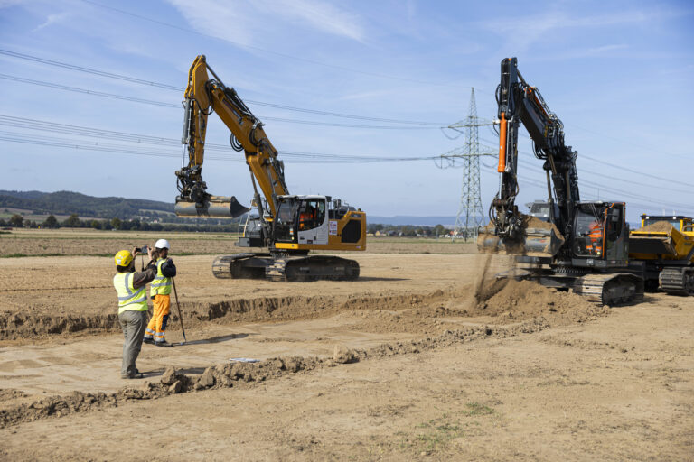 Archäologen stehen auf einer Baustelle von „TransnetBW“ beim Bauauftakt von „SuedLink“ und beobachten während einer archäologischen Voruntersuchung des Bodens, wie ein Bagger Erdschichten abträgt. Foto: picture alliance/dpa/Michael Matthey