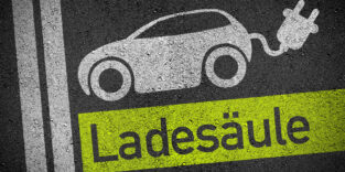 Auf Asphalt ist ein Elektroauto aufgemalt, aus dem am Heck ein Stecker schaut. Darunter steht das Wort Ladesäule.