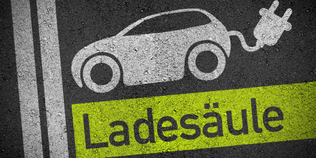 Auf Asphalt ist ein Elektroauto aufgemalt, aus dem am Heck ein Stecker schaut. Darunter steht das Wort Ladesäule.