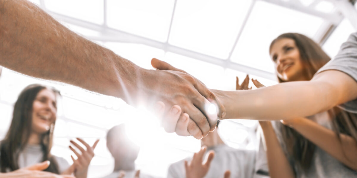 Zwei Personen schütteln sich die Hände, während eine Gruppe von Menschen drumherum in die Hände klatscht