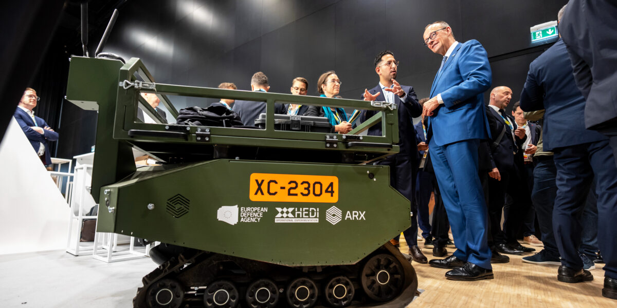 Bundeskanzler Friedrich Merz (CDU, Mitte r) lässt sich von Marc Wietfeld (M), CEO von ARX Robotics, ein ferngesteuertes Transportfahrzeug bei der Wiederaufbaukonferenz für die Ukraine erklären