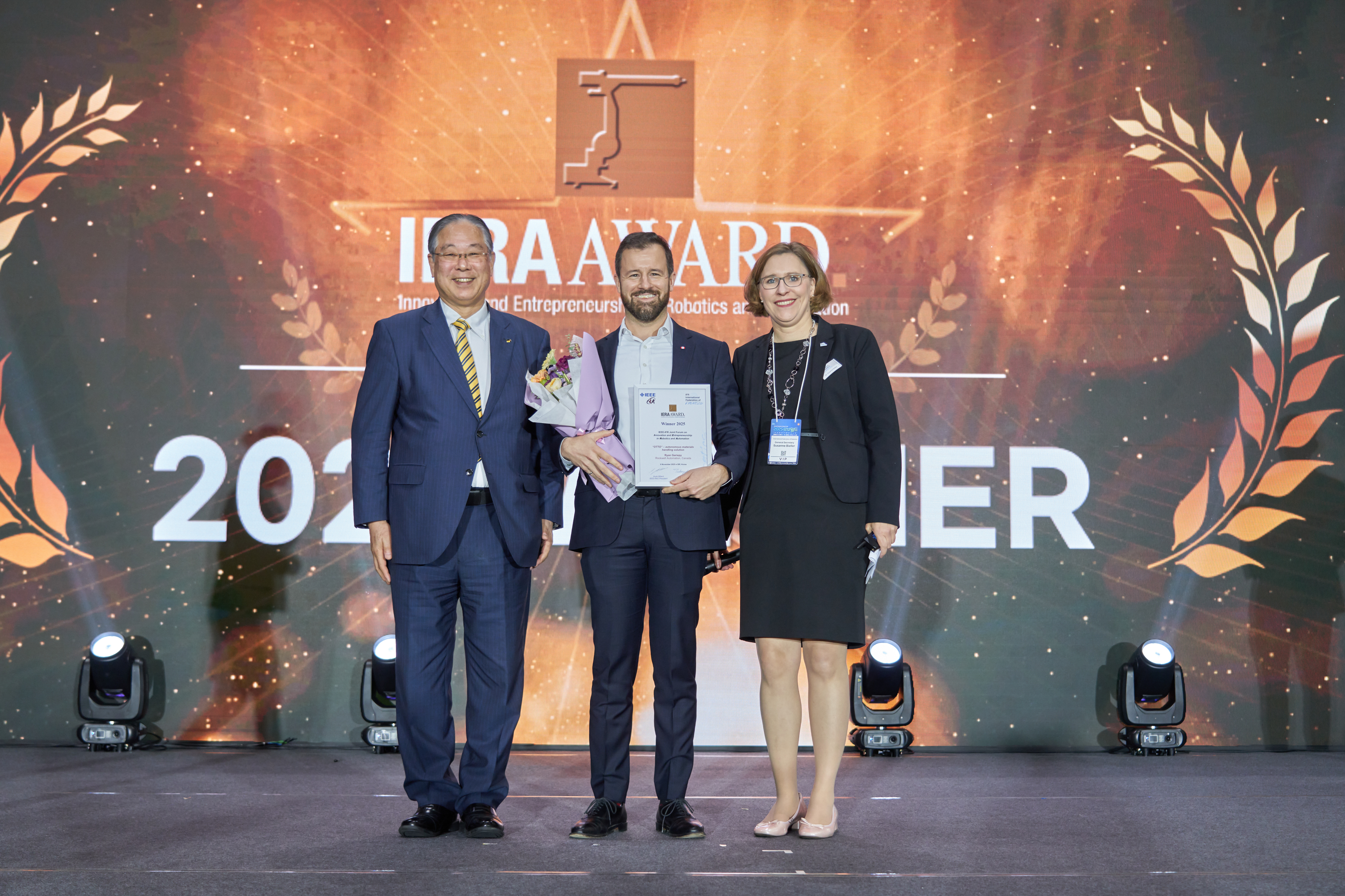 Die Verleihung des IERA Award 2025 (von links nach rechts): Takayuki Ito, IFR President; Ryan Gariepy, Rockwell Automation; Susanne Bieller, IFR General Secretary. Foto: KAR