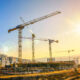 Large construction site including several cranes, with clear sky and the sun