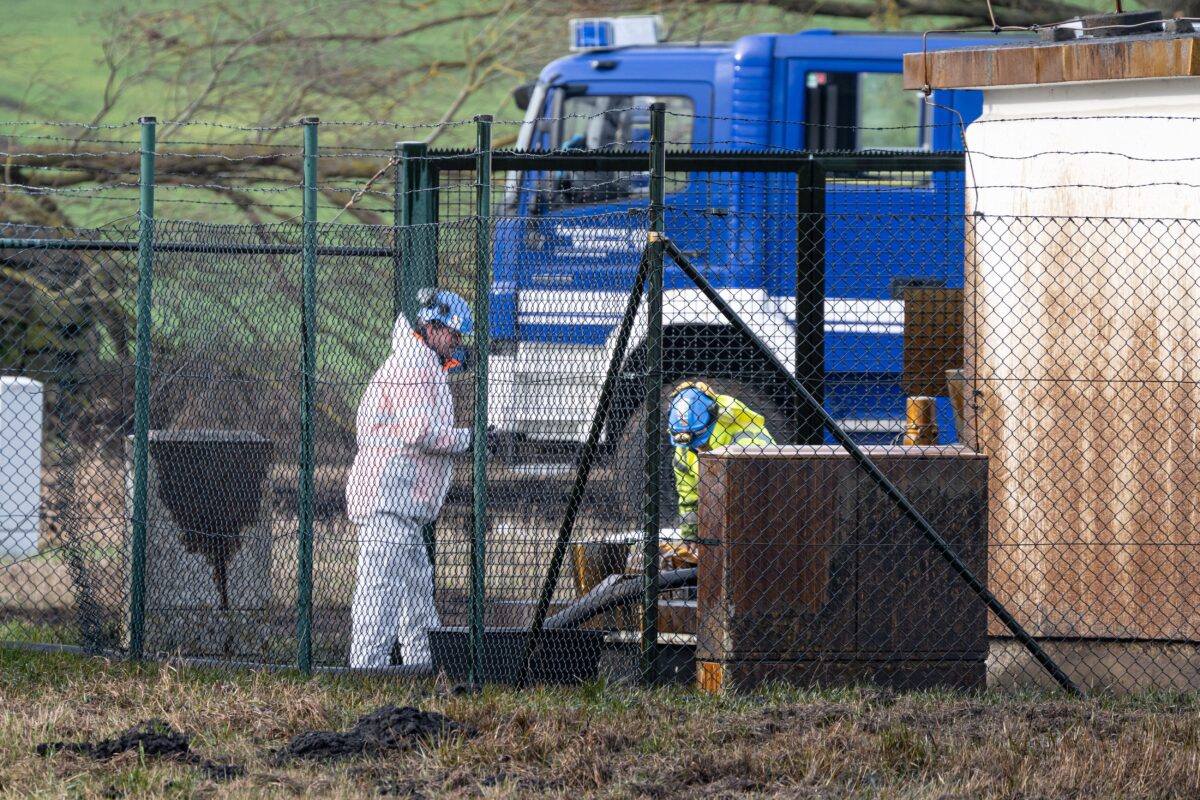 Arbeiter in weißem Schutzanzug an der eingezäunten Schieberstation bei Gramzow, daneben ein blauer Saugwagen.