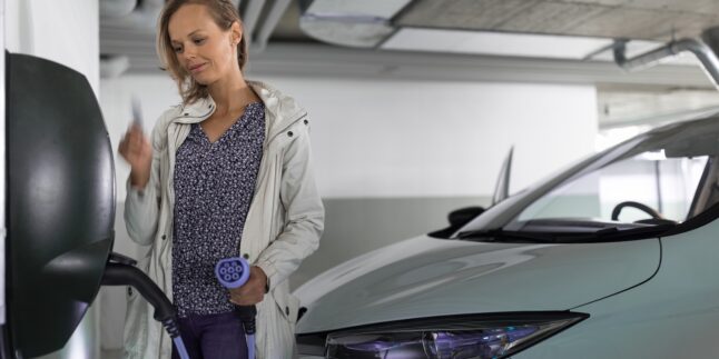 Frau steht mit einer Ladekarte in einer Tiefgarage vor einer Ladebox, das Kabel ist bereits mit dem Auto verbunden.