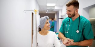 Krebspatientin geht mithilfe eines Pflegers über einen Gang.