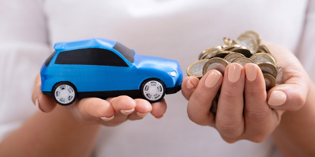 Eine Frau hält in ihren Händen ein blaues Modellauto und eine Handvoll Euro-Münzen.