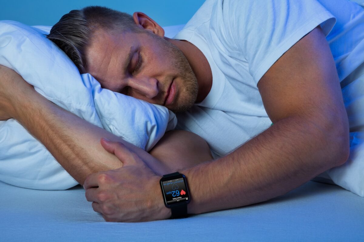 Mann liegt im Bett und schläft. Die Smartwatch an seinem linken Handgelenk überwacht seinen Schlaf.