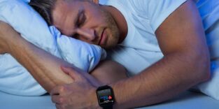 Mann liegt im Bett und schläft. Die Smartwatch an seinem linken Handgelenk überwacht seinen Schlaf.