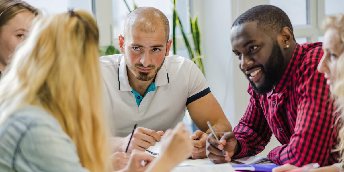 Junge Erwachsene sitzen gemeinsam an einem Tisch, diskutieren und arbeiten konzentriert an Unterlagen – Teamarbeit und Ideenaustausch in einer Lernumgebung.