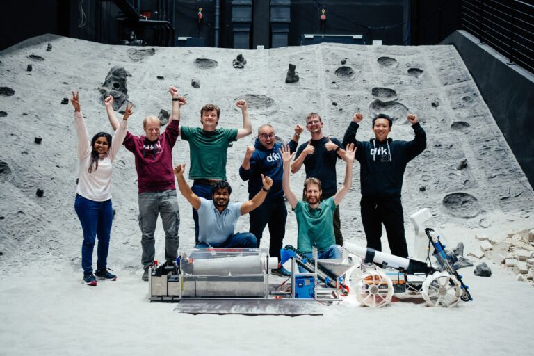 Vor dem künstlichen Mondkrater des DFKI: Das erfolgreiche Team BREMEN und sein Gewinner-System der ESA Space Resources Challenge 2025. Foto: DFKI, Jimmy Dao Sheng Liu