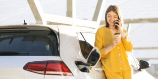 Frau lädt ihr E-Auto und telefoniert