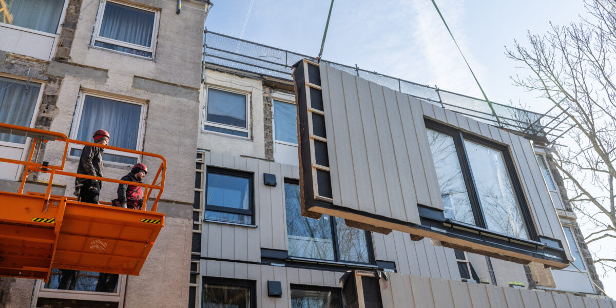 Arbeiter montieren ein bereits vormontiertes Fassadenteil an ein Wohnhaus