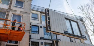 Arbeiter montieren ein bereits vormontiertes Fassadenteil an ein Wohnhaus