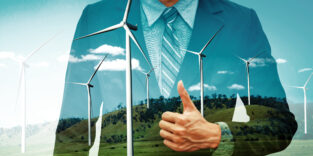 Ein Mann zeigt Dauen hoch, im Hintergrund sind die Windräder zu sehen.