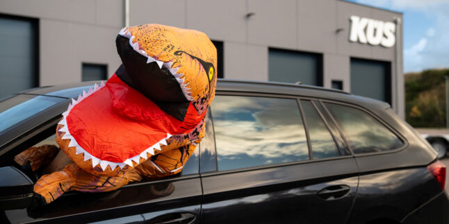 Eine Person im Dinosaurier-Kostüm schaut aus einem Autofenster.