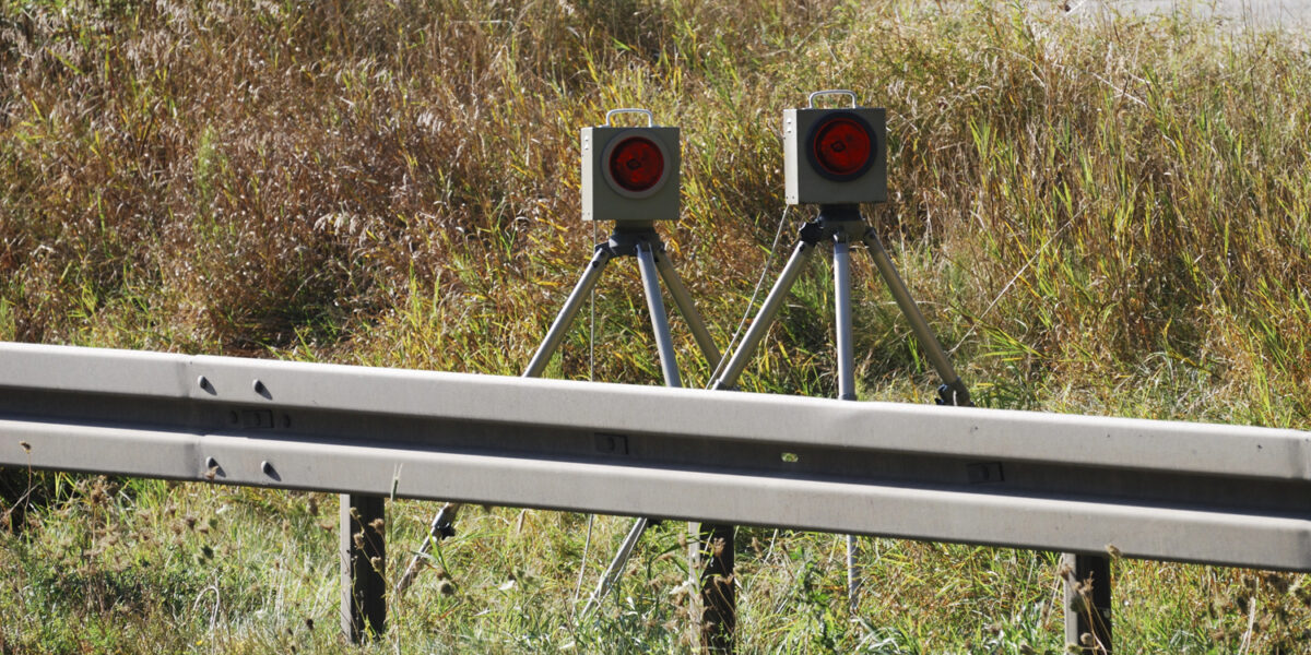 Eine Radarfalle hinter einer Leitplanke.