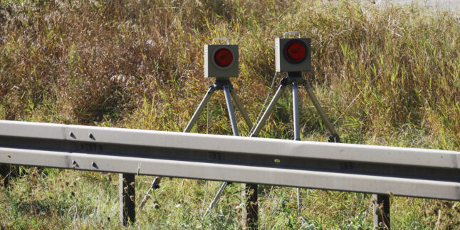 Eine Radarfalle hinter einer Leitplanke.