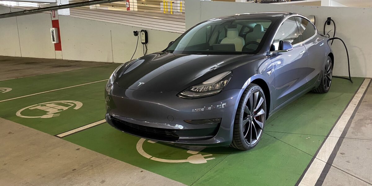 A gray Tesla Model 3 charging at a free garage charging station.