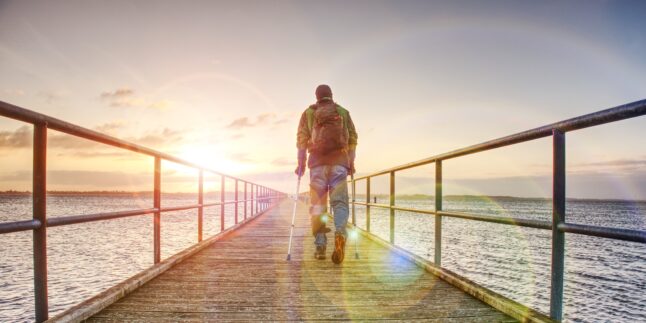 Ein Mann mit Krücken am Meer.
