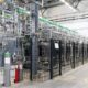 Blick in die Elektrolyseurhalle von BASF in Ludwigshafen: Hinter Schutzgittern stehen mehrere PEM-Elektrolyseur-Module, verbunden durch ein Netz aus Rohrleitungen und Versorgungsleitungen. Mit 54 MW Leistung ist es derzeit die größte PEM-Elektrolyseanlage in Deutschland.