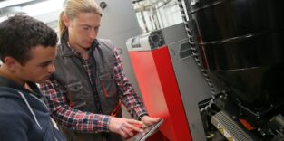 Junger Mann in der Berufsausbildung misst die Temperatur einer Wärmepumpe.