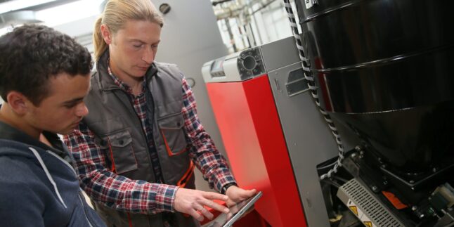 Junger Mann in der Berufsausbildung misst die Temperatur einer Wärmepumpe.