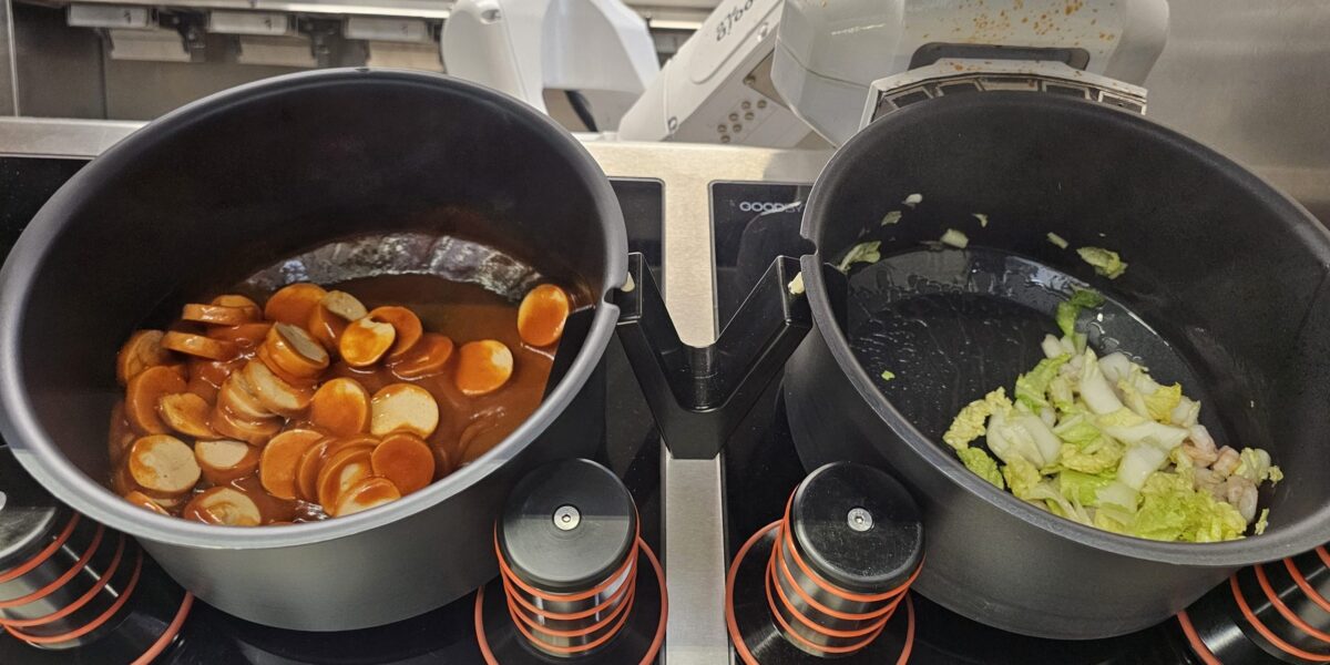 Ein Roboterarm kocht mit zwei Töpfen unterschiedliche Gerichte.