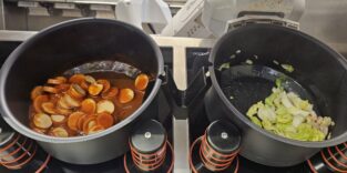 Ein Roboterarm kocht mit zwei Töpfen unterschiedliche Gerichte.