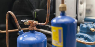 Zu sehen sind Teile eines Kühlkreislaufs einer Klimaanlage. Dazu gehören Kupferrohre und blaue Druckbehälter.