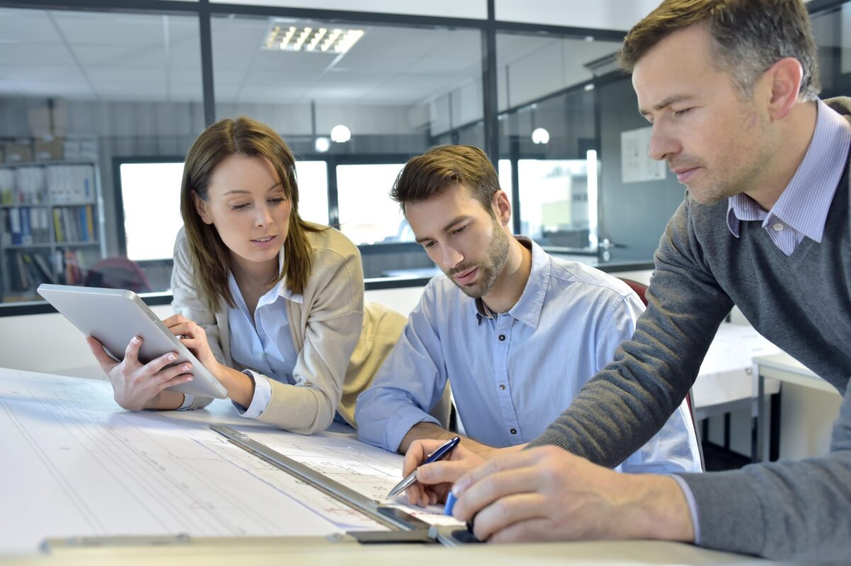zwei Männer und eine Frau sitzen am Schreibtisch und grübeln über einem Problem