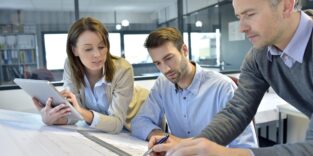 zwei Männer und eine Frau sitzen am Schreibtisch und grübeln über einem Problem