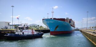 Ein Containerschiff wird von einem Schlepper in eine Neopanamax-Schleuse des Panamakanal manövriert