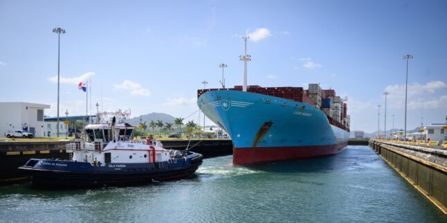 Ein Containerschiff wird von einem Schlepper in eine Neopanamax-Schleuse des Panamakanal manövriert