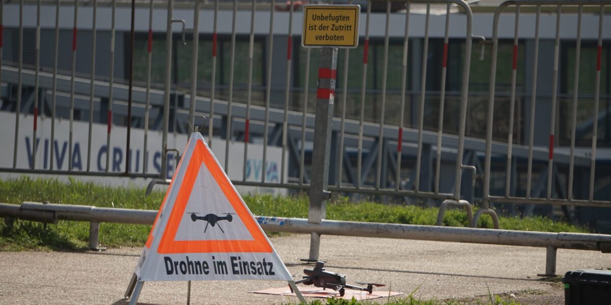 Auf dem Startplatz einer kleinen Drohne am Rhein ist ein Warnschild mit der Aufschrift "Drohne im Einsatz" zu sehen.