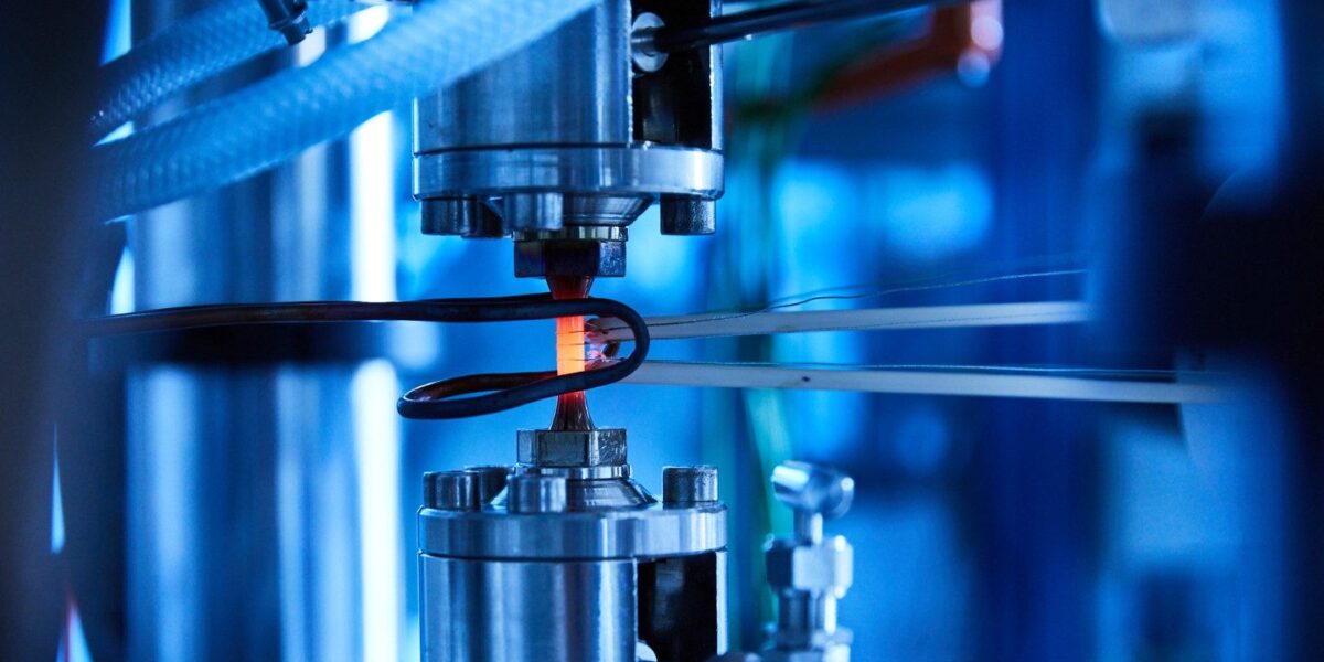 Glühende Werkstoffprobe in einer Prüfmaschine, blau beleuchtetes Labor am Fraunhofer IWM